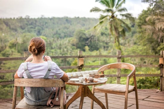 a woman is sitting at a table on a balcony overlooking a forest .