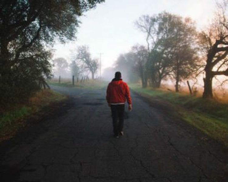 a man in a red jacket is walking down a foggy road .