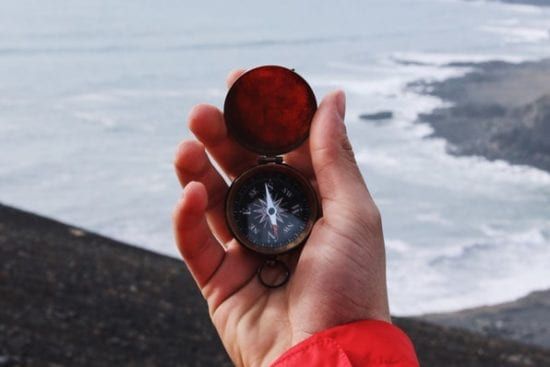 a person is holding a compass in their hand in front of the ocean .