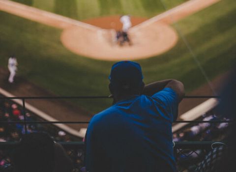 a man in a blue shirt is watching a baseball game from the stands .
