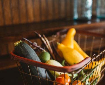 a basket filled with vegetables is sitting on a wooden table .