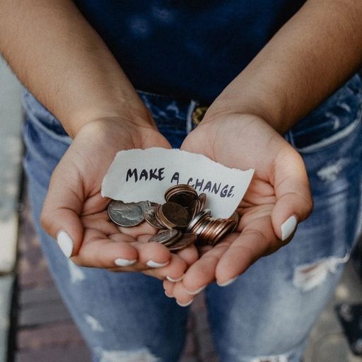 a woman is holding a pile of coins and a piece of paper that says `` make a change '' .