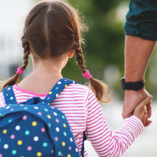a little girl with a backpack is holding a man 's hand .