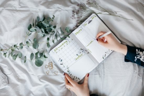 a person is writing in a notebook on a bed .