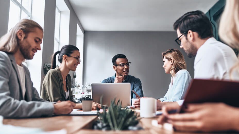 a group of people are sitting around a table with laptops .