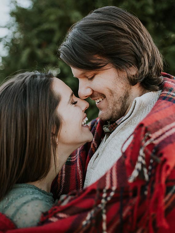 a man and a woman are looking into each other 's eyes while wrapped in a plaid blanket .