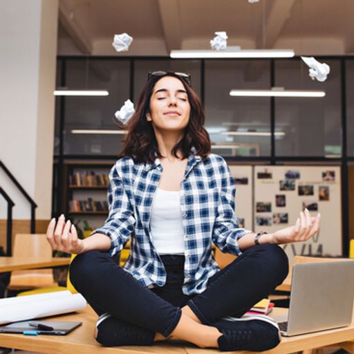 a woman is sitting in a lotus position at a desk with a laptop .