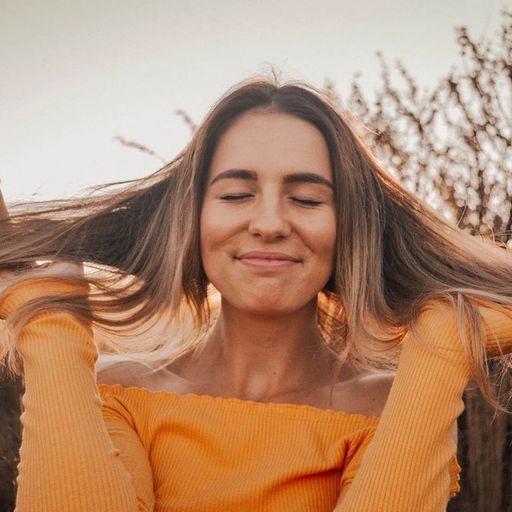 a woman in a yellow shirt is holding her hair in a field .