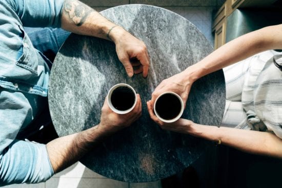 a man and a woman are sitting at a table holding cups of coffee .