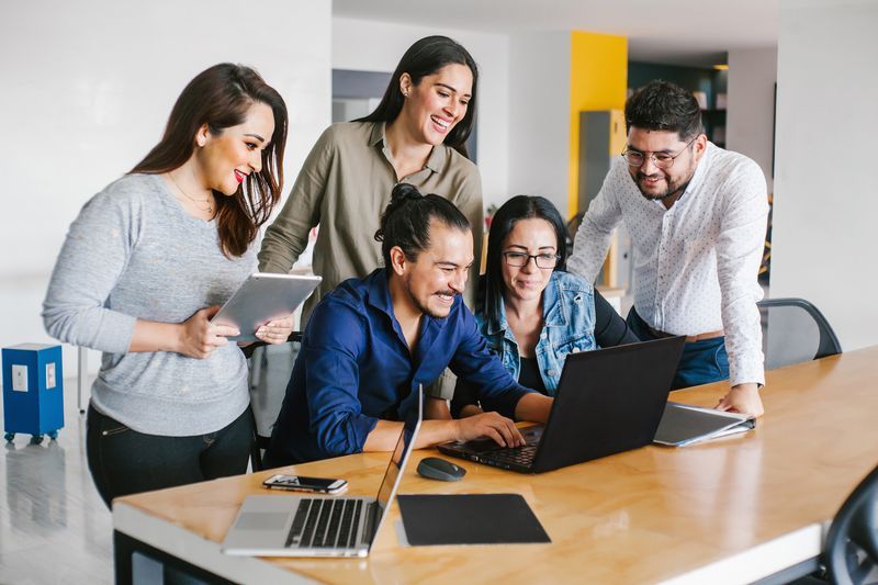 a group of people are standing around a table looking at a laptop computer .