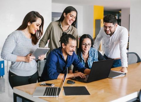 a group of people are standing around a table looking at a laptop computer .