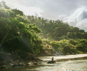 a man is sitting on a rock in the middle of a river .