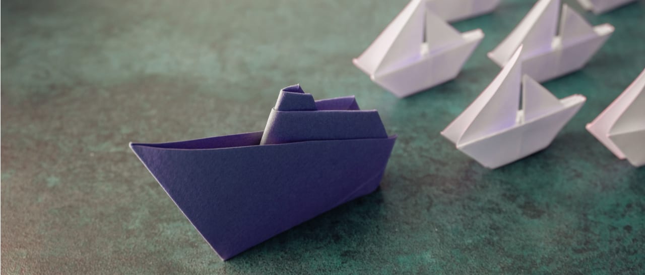 a purple paper boat is leading a row of white paper boats .