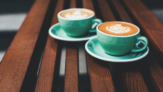 two cups of cappuccino are sitting on a wooden table .