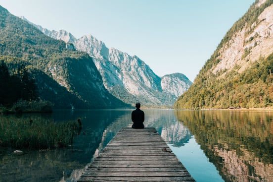 a man is sitting on a dock overlooking a lake with mountains in the background .
