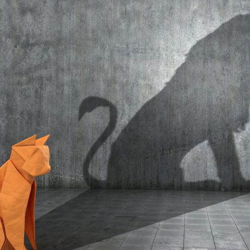 an origami cat is sitting in front of a wall with a shadow of a lion on it .