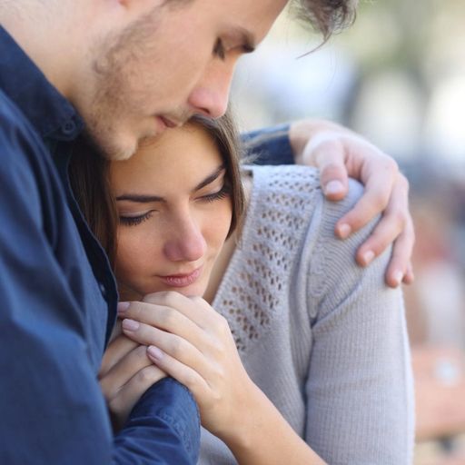 a man is comforting a woman who is sitting on a bench .
