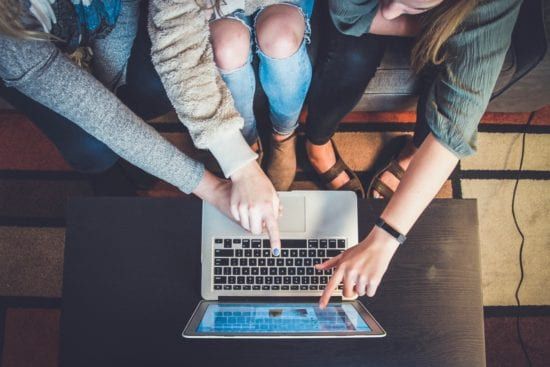 three women are sitting on a couch looking at a laptop computer .