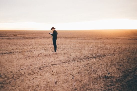 a man is standing in a field reading a book .