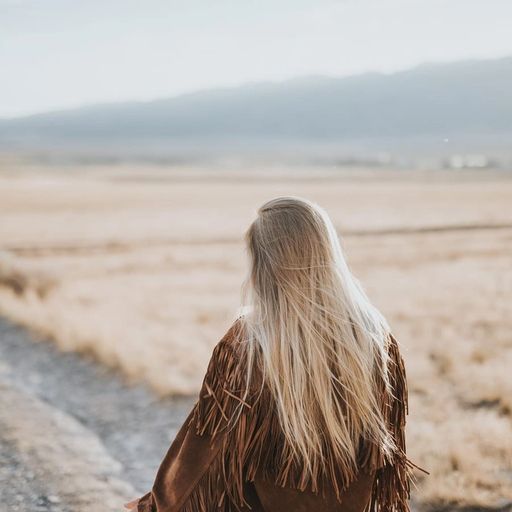 a woman is sitting on the side of a dirt road in the middle of a field .