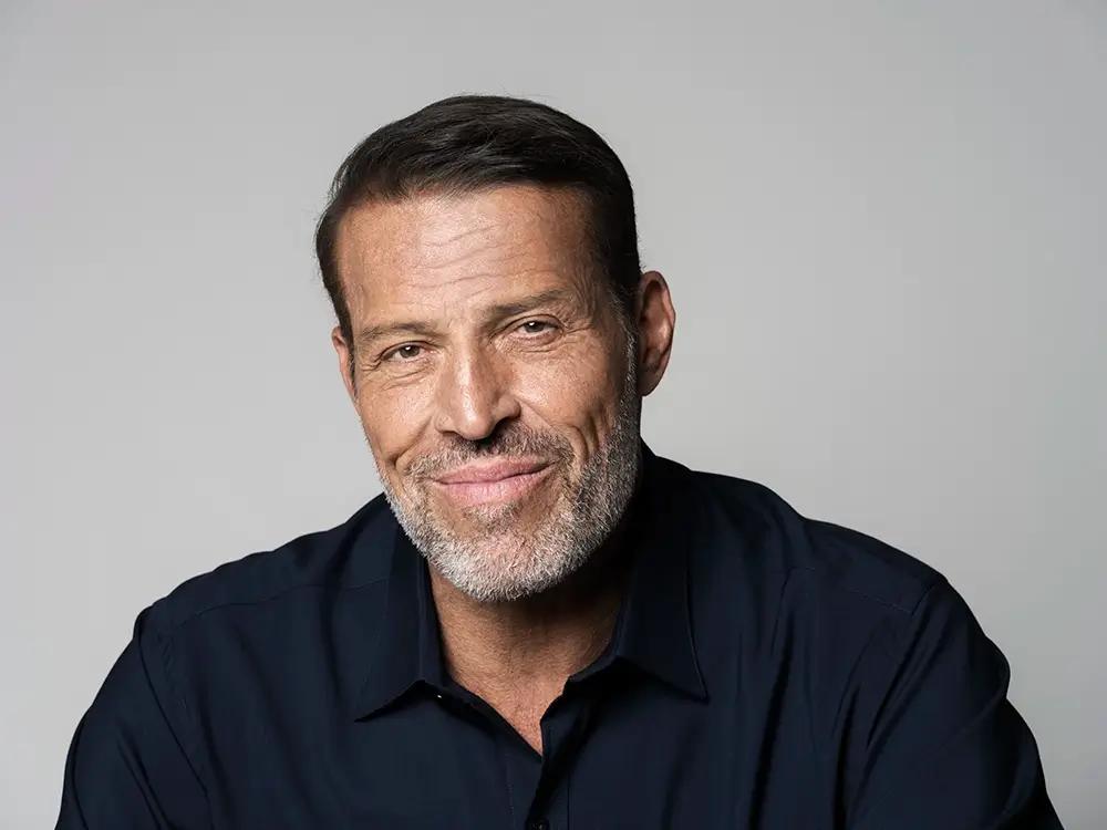 Tony Robbins smiling with a salt-and-pepper beard and dark shirt.
