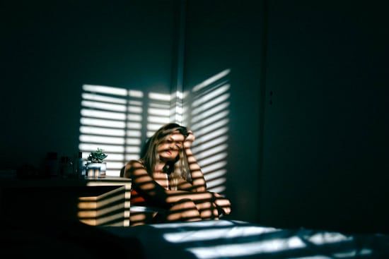 a woman is sitting on a bed in front of a window with blinds .