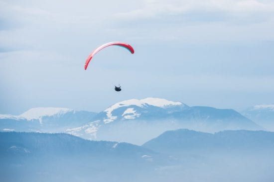 a person is parasailing over a snowy mountain range .