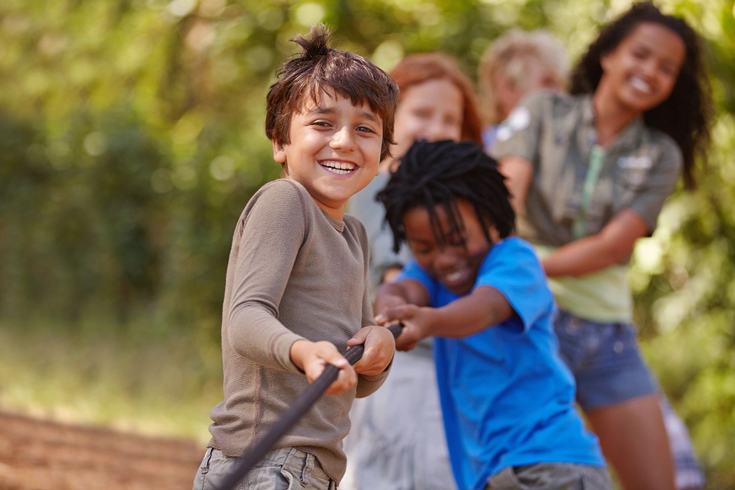 Diverse group of smiling children playing tug-of-war outdoors.