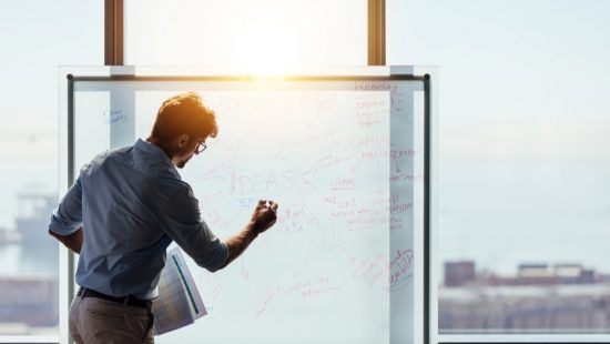 a man is writing on a whiteboard in front of a window .