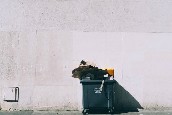 a garbage can is sitting on the sidewalk in front of a white wall .