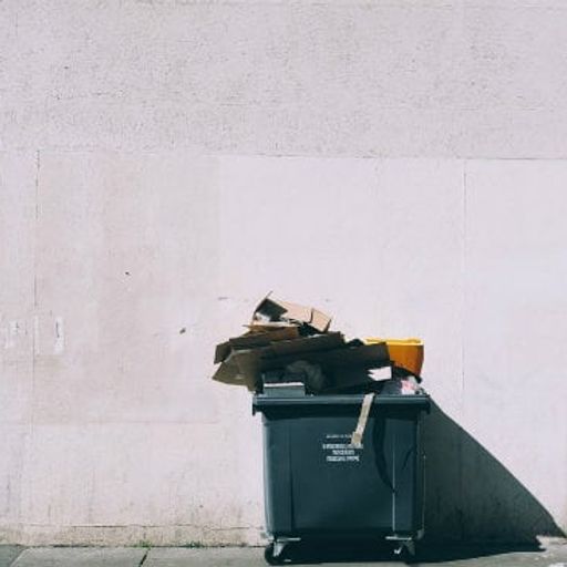 a garbage can is sitting on the sidewalk in front of a white wall .