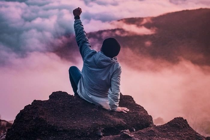 a man is sitting on top of a rock with his fist in the air .