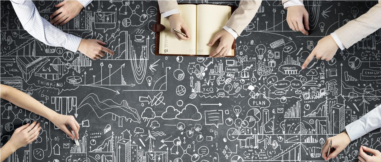 a group of people are sitting around a table looking at a chalkboard with drawings on it .