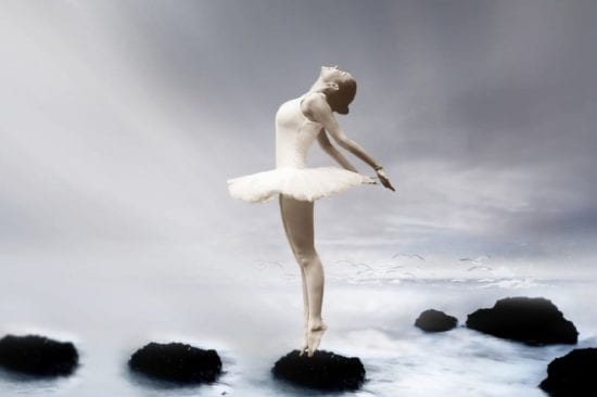 a ballerina is standing on a rock in the water .