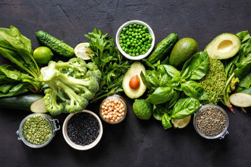 a variety of green vegetables and beans on a black table .