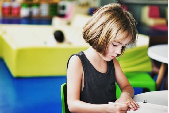 a little girl is sitting at a table writing on a piece of paper .