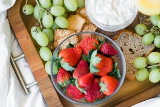a wooden tray topped with strawberries , grapes , crackers and yogurt .
