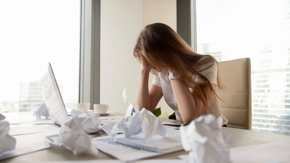 a woman is sitting at a desk with crumpled papers and a laptop .