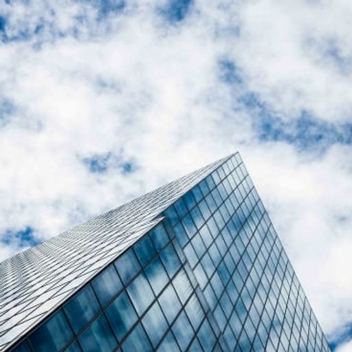 looking up at a tall building with a blue sky and clouds in the background .