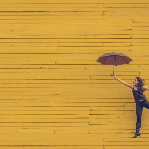 a woman is holding an umbrella in front of a yellow wooden wall .