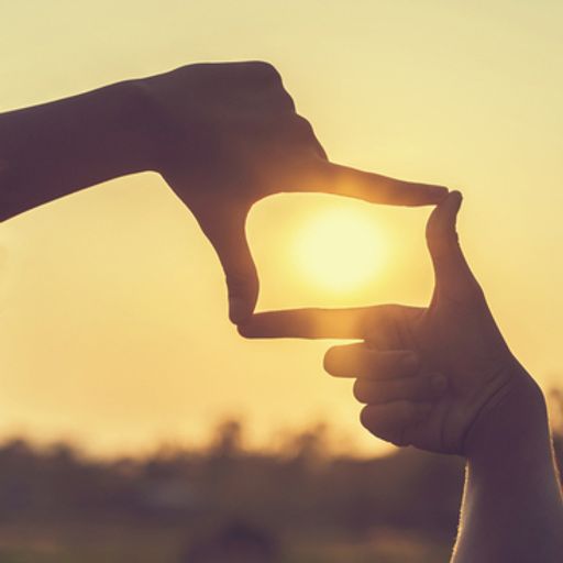 a woman is looking at the sun through a frame made of her hands .