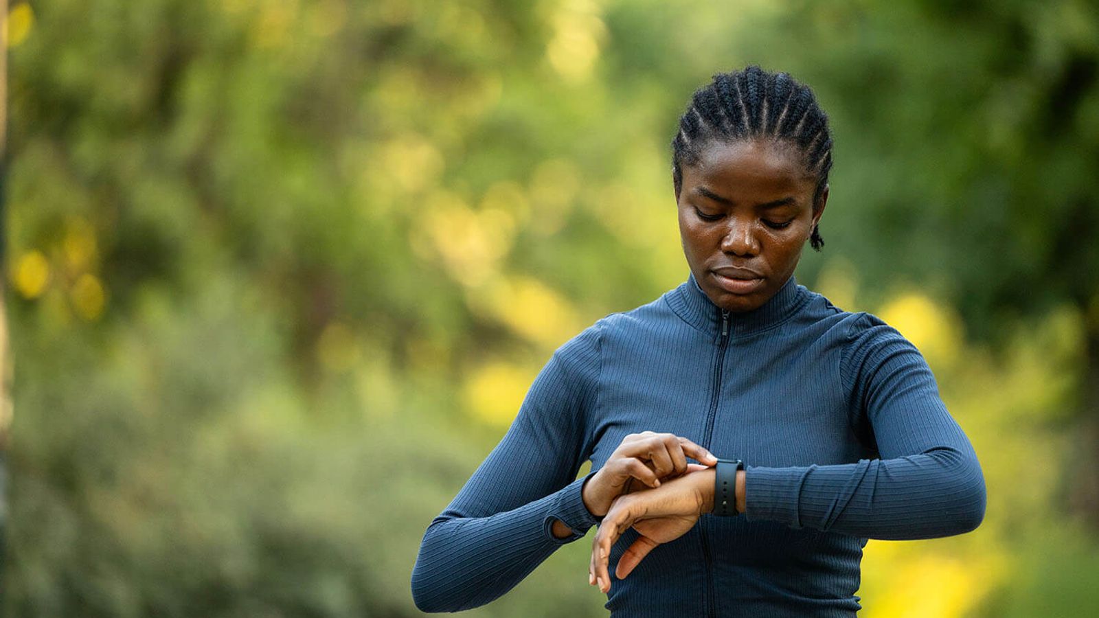 A Black woman in athletic wear checks her smartwatch outdoors.