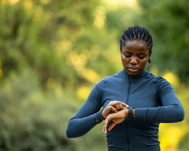 A Black woman in athletic wear looks at her smartwatch outdoors.
