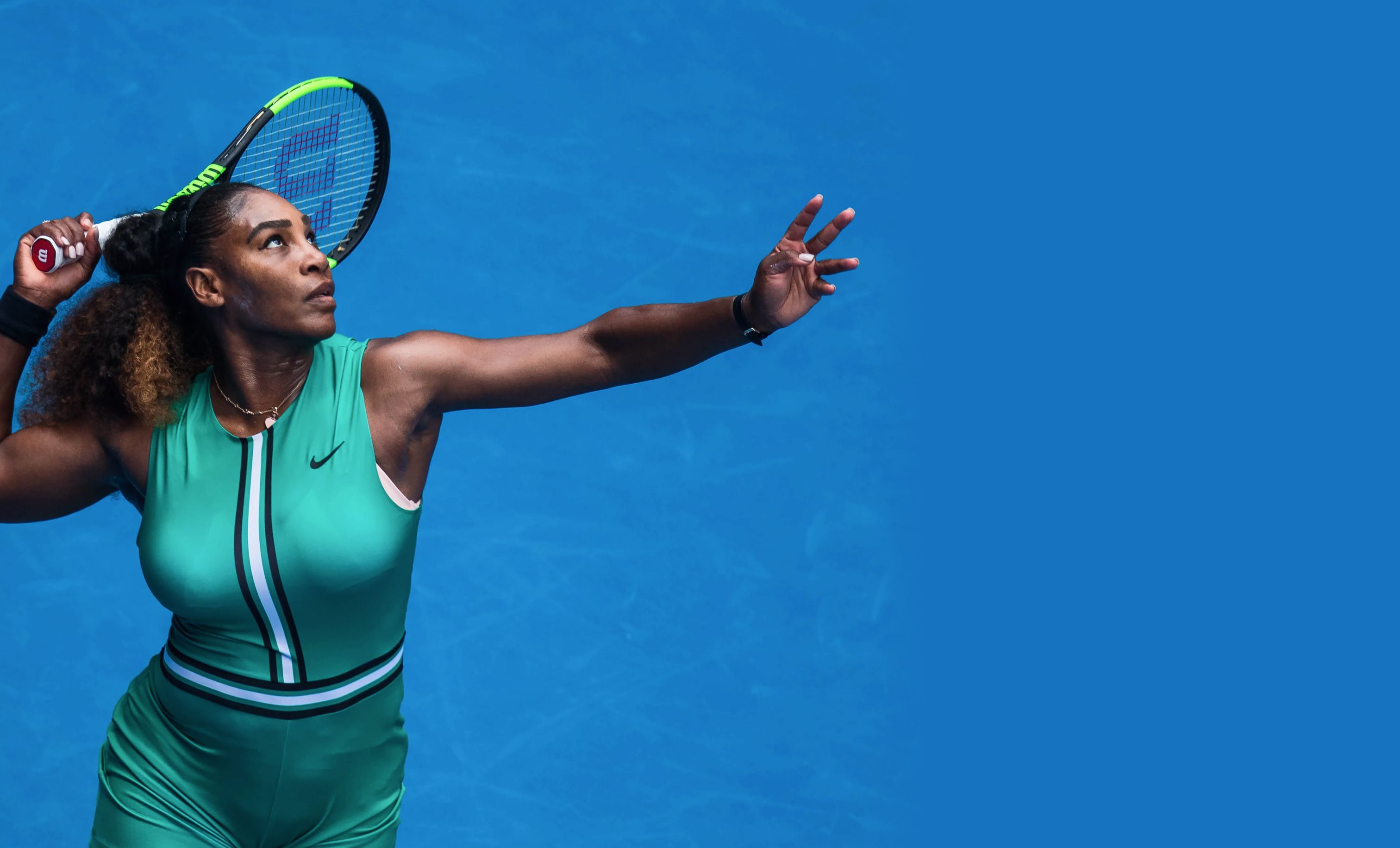 Serena Williams is holding a tennis racquet in front of a blue wall
