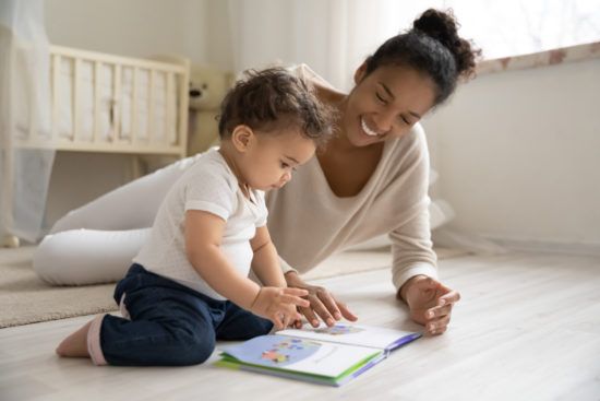 a woman is sitting on the floor reading a book to her baby .