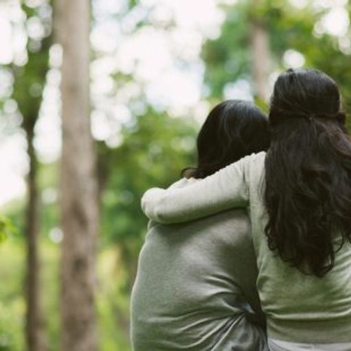 two women are hugging each other in the woods .