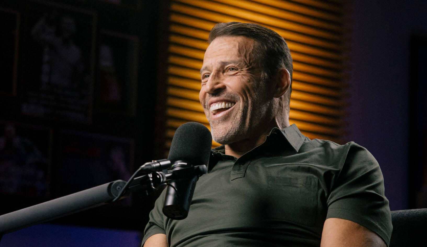 a man in a blue jacket is smiling in front of a stone wall