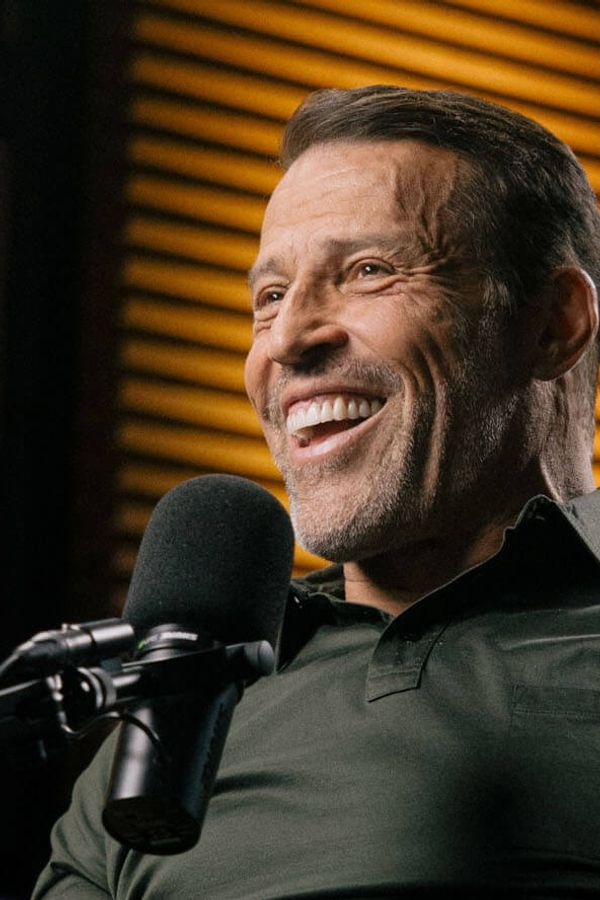 a man in a blue jacket is smiling in front of a stone wall