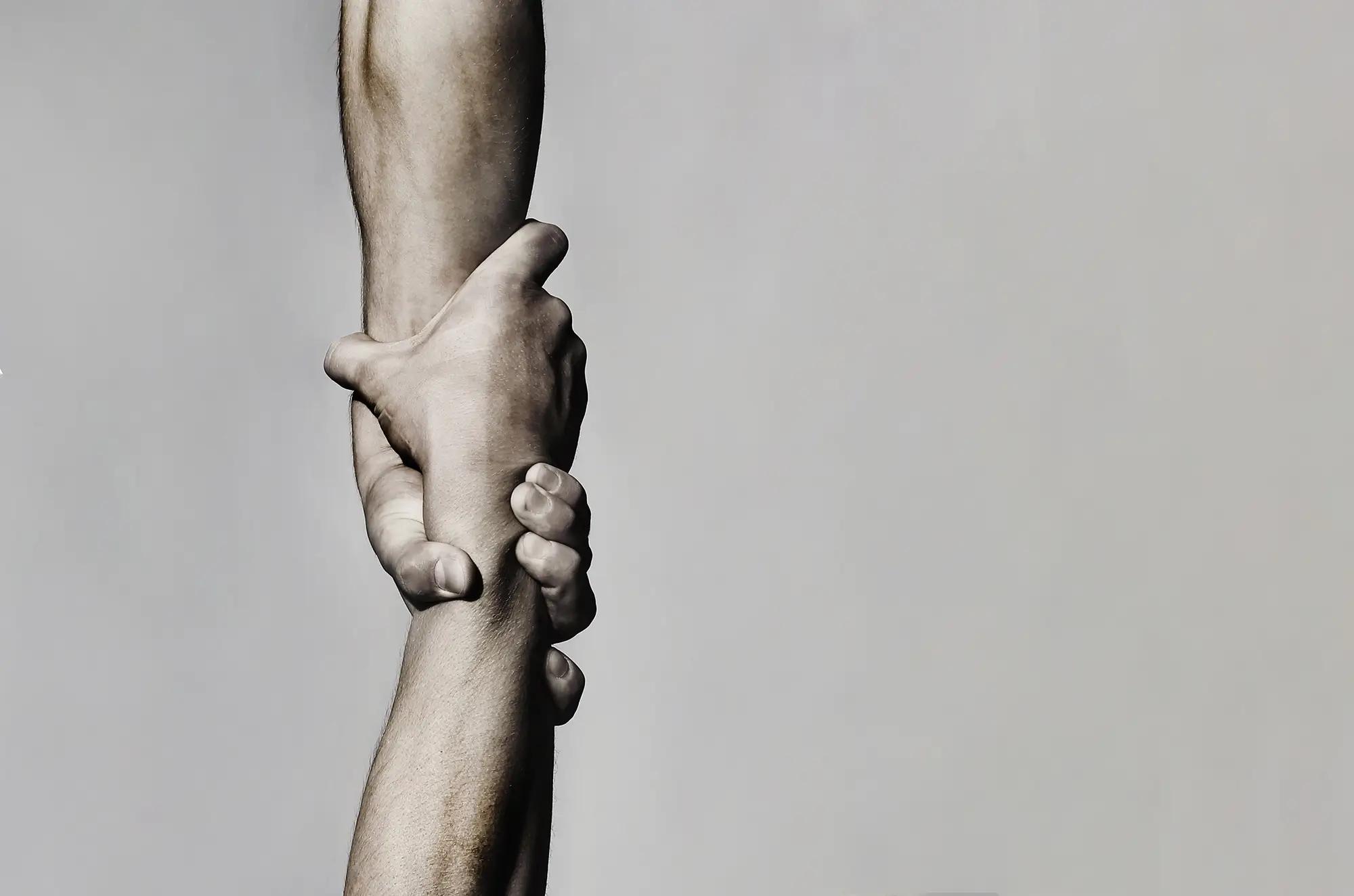 Two hands firmly grasp each other's forearms, symbolizing help and support.