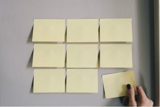 a person is holding a piece of paper next to a bunch of sticky notes on a wall .
